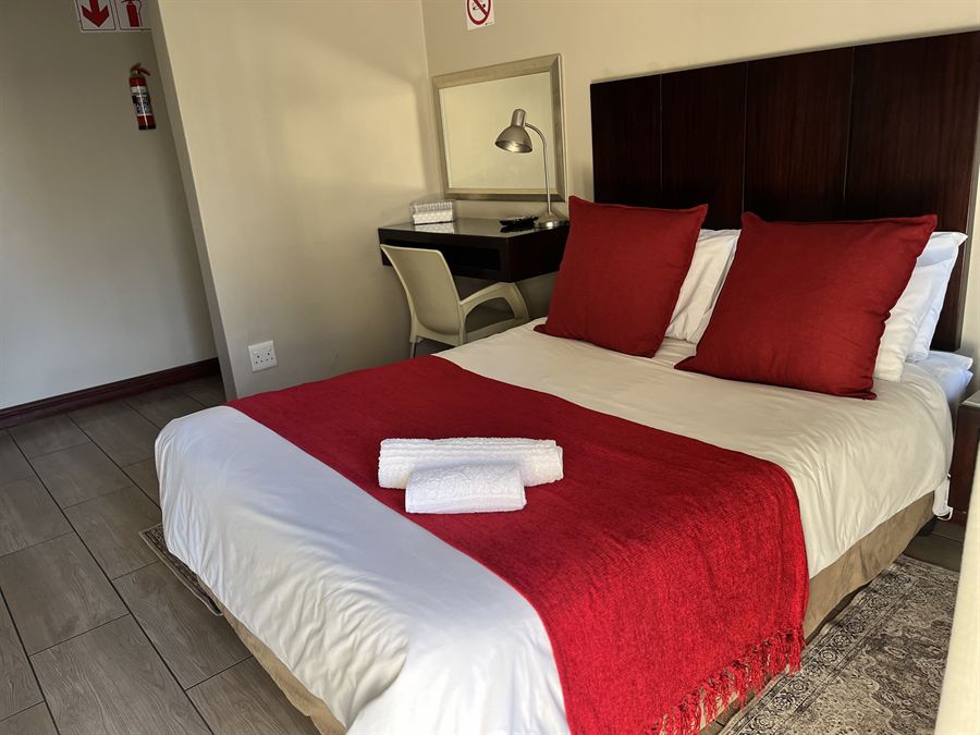 Double bed with red throw and dark wood headboard in the Standard Double Room at Cozy Corner Brandwag
